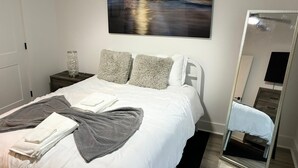 Un dormitorio ordenado con cama, almohadas, una mesita de noche con lámpara y un espejo grande.