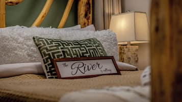 A neatly made bed with a pillow, a sign reading "The River is calling," and a lamp in the background.