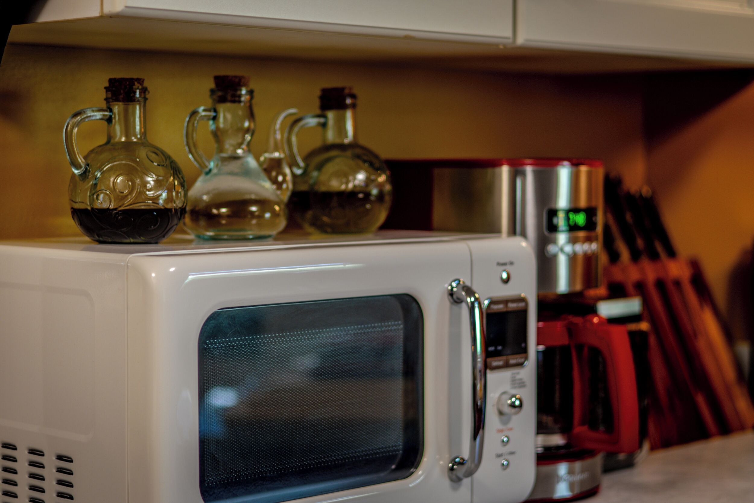 Un horno microondas con pantalla digital y una cafetera roja sobre la encimera.