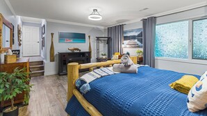 Un dormitorio con una cama grande, un escritorio, una silla, una planta en maceta y una ventana con vistas a un paisaje nevado.