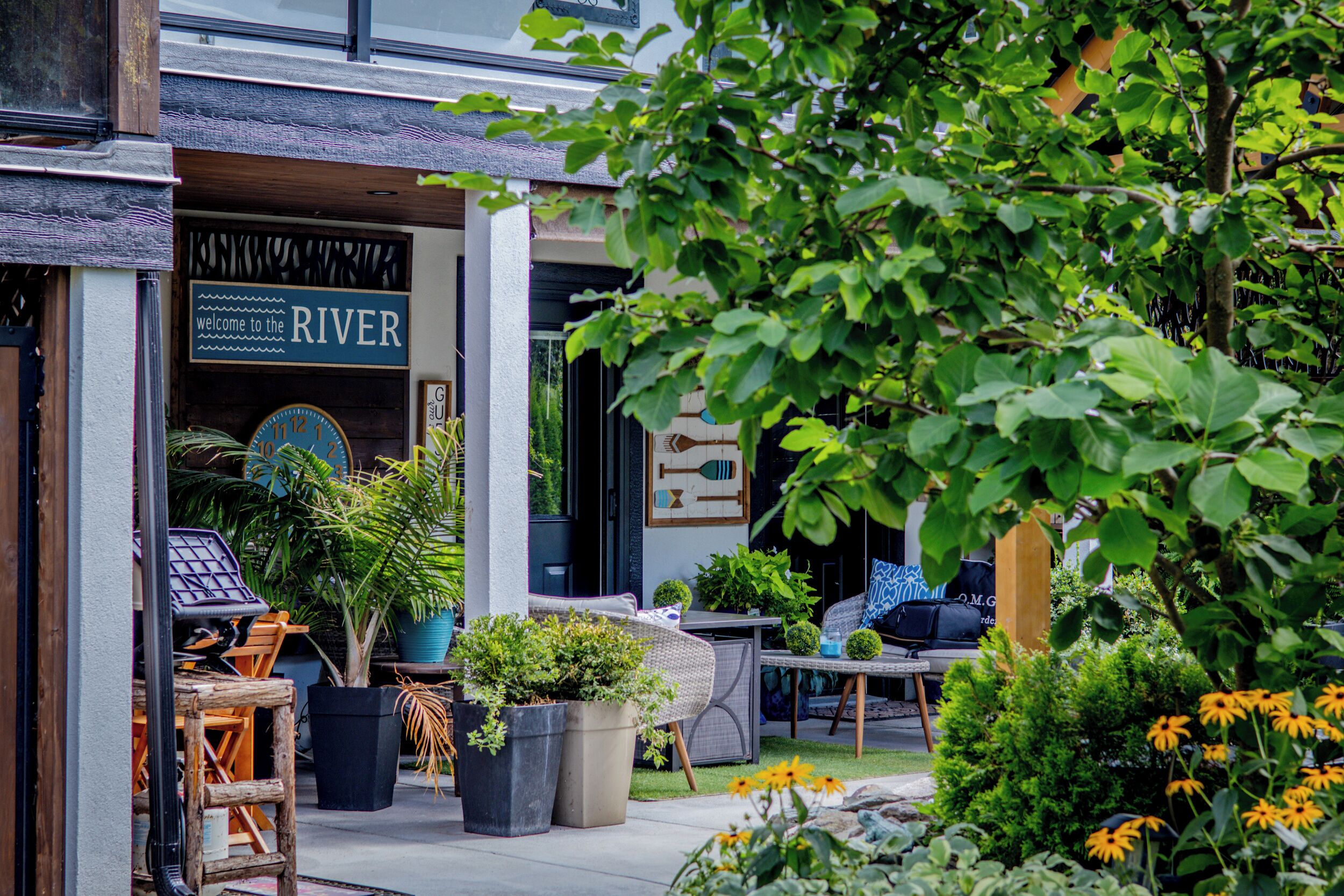 An outdoor seating area with wicker furniture, potted plants, and a sign reading "welcome to the RIVER".