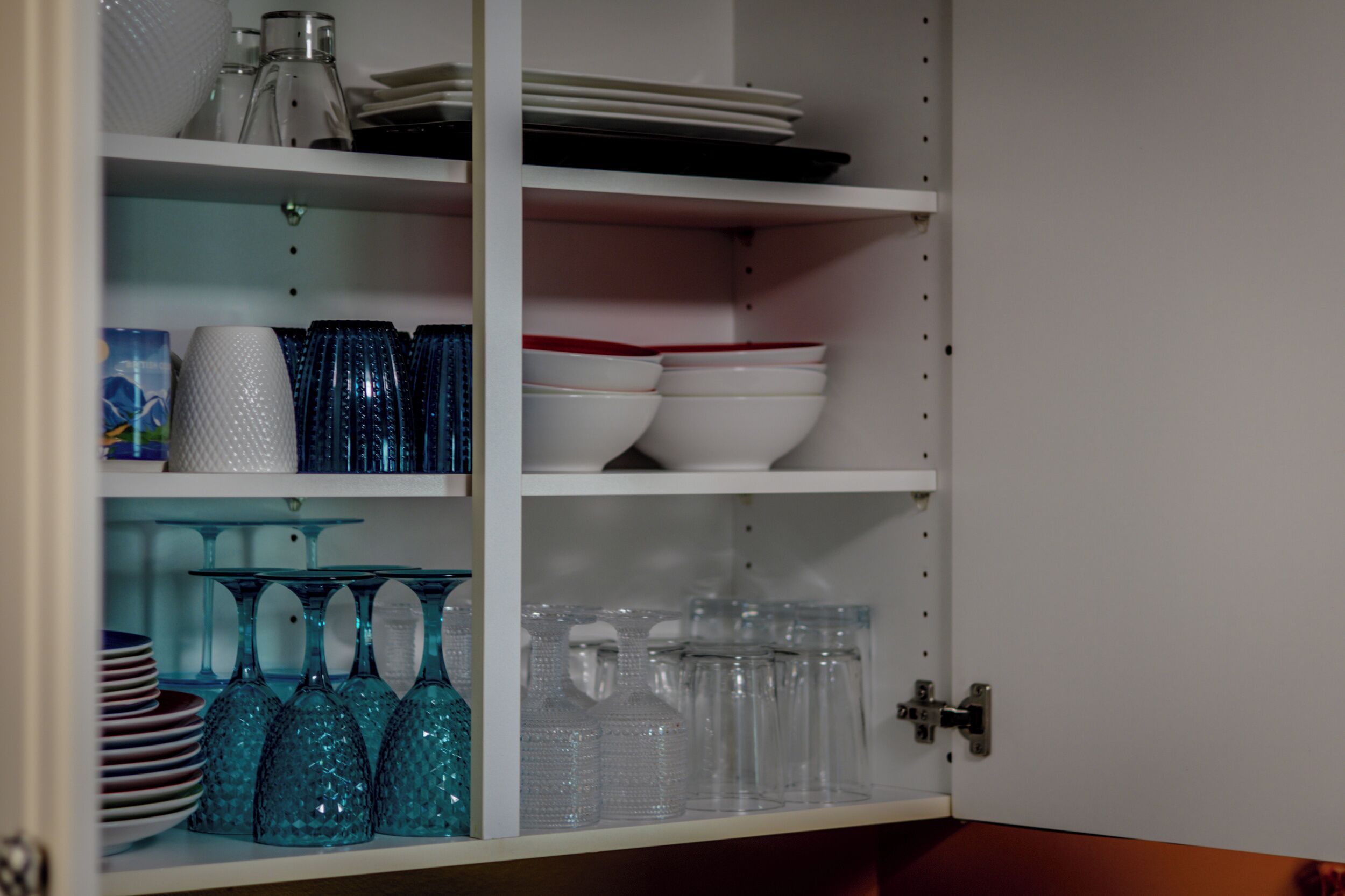 A kitchen cabinet with shelves holding various glassware and dishes.
