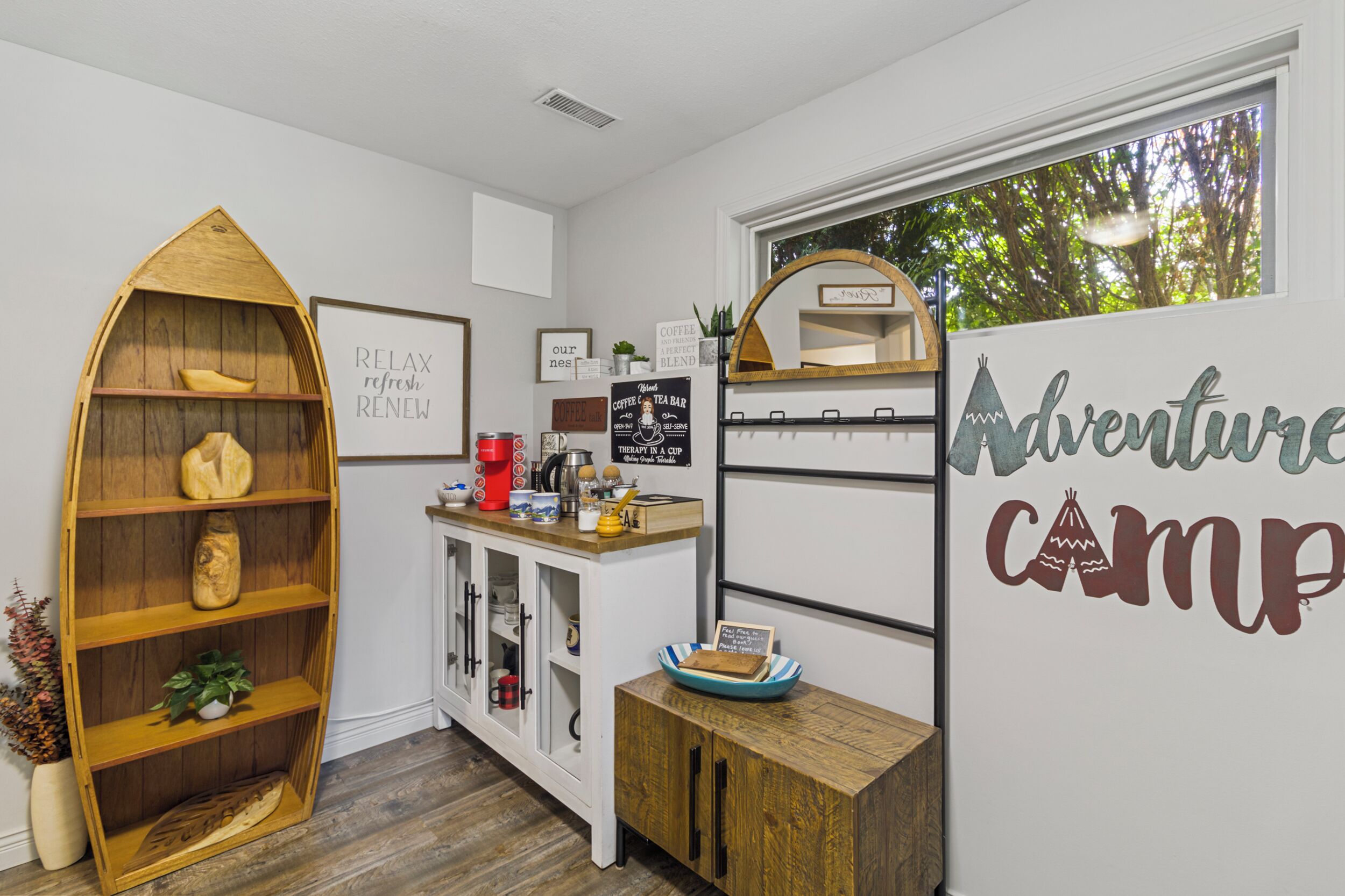 Eine gemütliche Küche mit einem Holzbottenschrank, einer Kaffeestation und einer Wand mit Dekoration zum Thema 'Adventure Camp'.