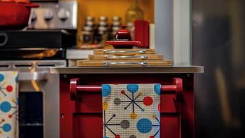 Eine Küche mit roter Arbeitsplatte, einem Holztisch zum Schneiden und einem Stoff mit geometrischem Muster, der an einem roten Haken hängt.