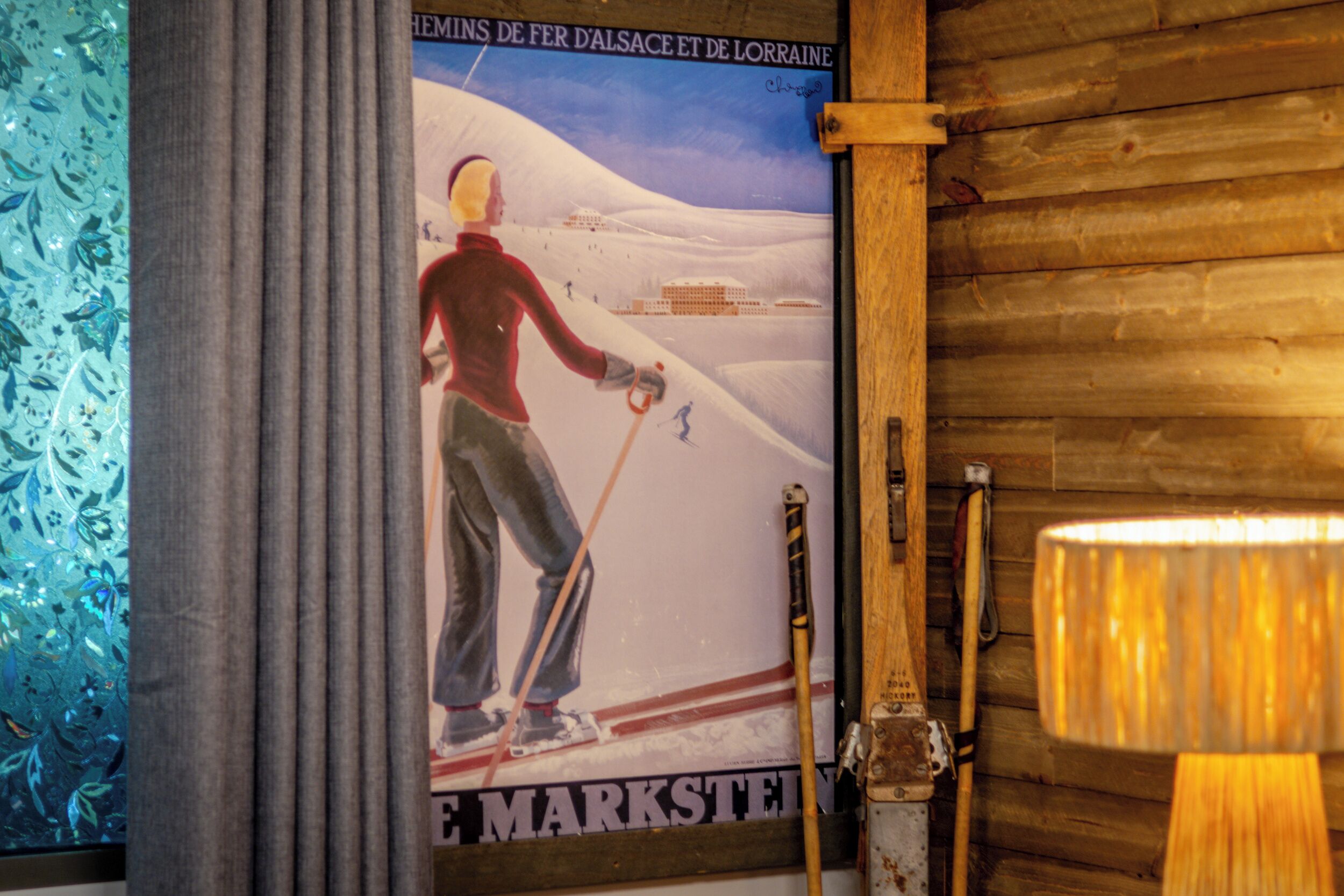 Une affiche représentant un skieur sur une montagne, un mur en bois et une lampe.
