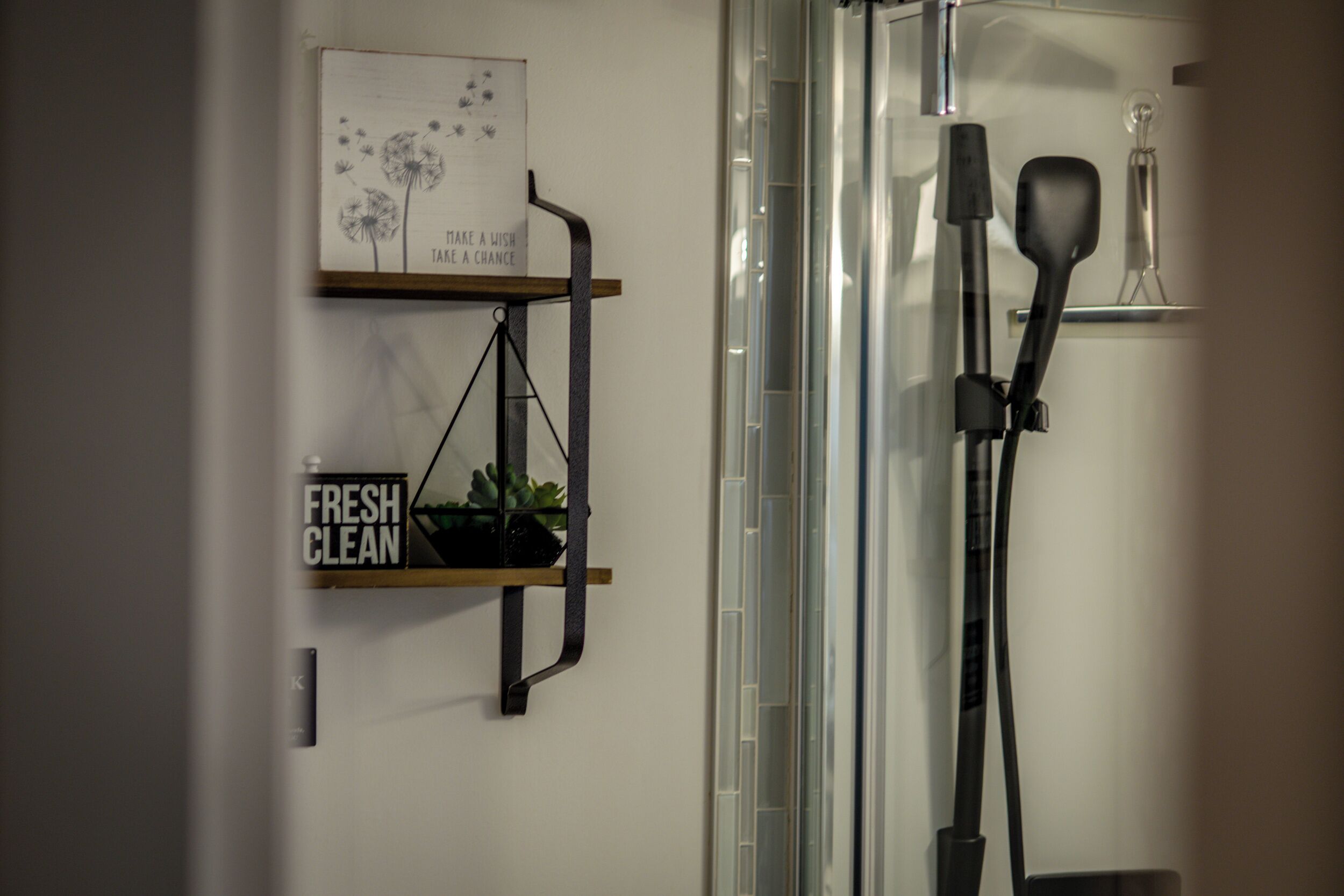Et badeværelse med bruser, spejl, hylde med skilt, der siger "FRESH CLEAN", og en plante.
