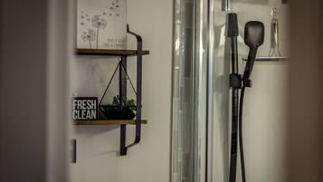 Et badeværelse med bruser, spejl, hylde med skilt, der siger "FRESH CLEAN", og en plante.