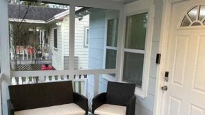 A porch with two dark-colored chairs and a small table, a white door, and a welcome mat. - Comfortable new 2- bedroom house (Jacksonville)