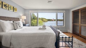A bedroom with a large bed, a window with a view of a lake and trees, and a flag. - Waterfront, Incredible Views and Private Dock! (Yarmouth)
