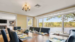 A dining area with a view of a lake, a chandelier, and a television in the background. - Waterfront, Incredible Views and Private Dock! (Yarmouth)