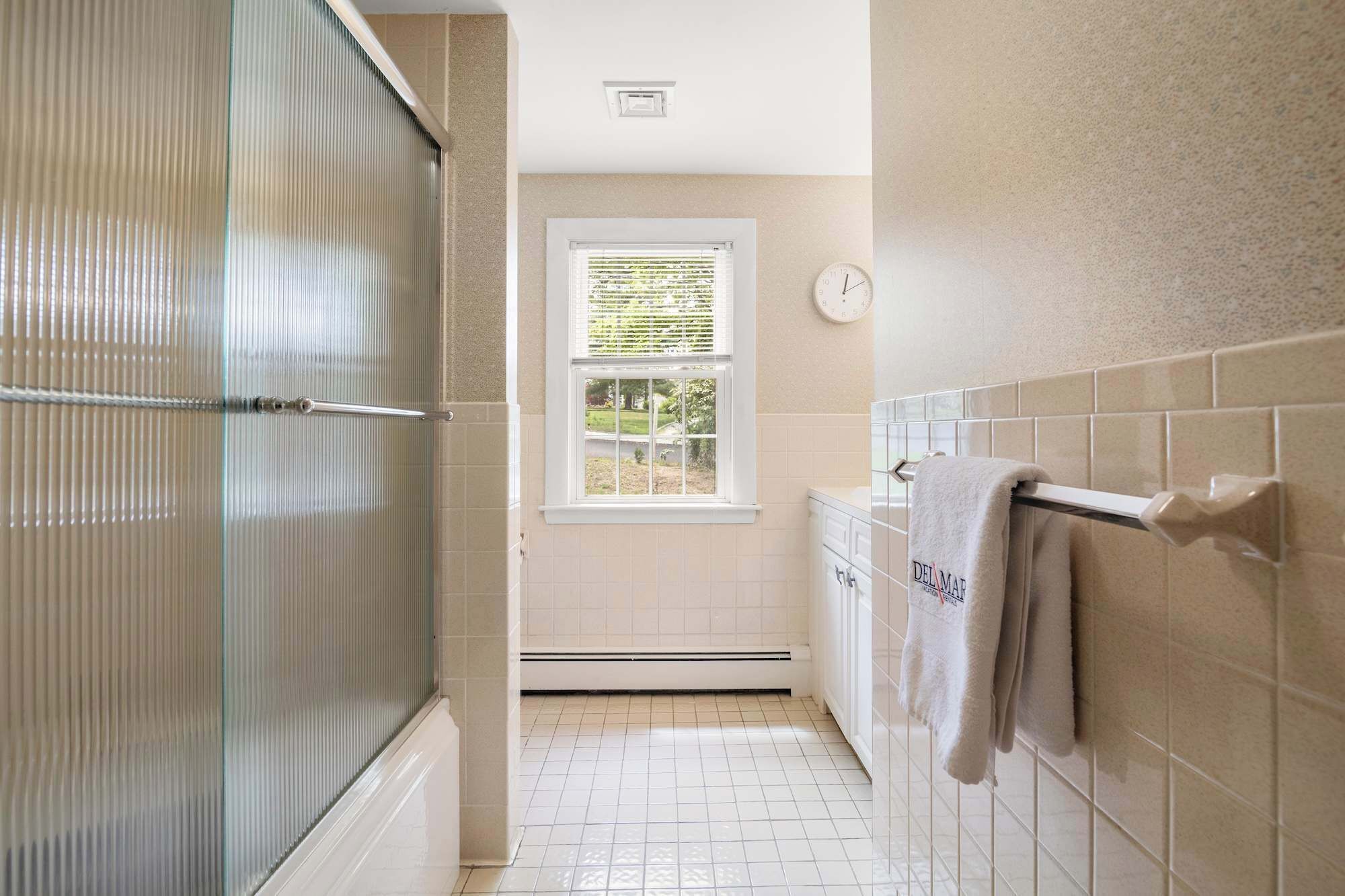 A bathroom with a shower, a window, a towel rack, and a wall-mounted clock.