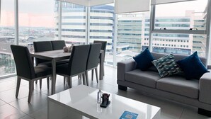 A modern living room with a dining area, large windows, and a city view.