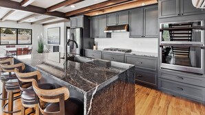 Une cuisine moderne avec des meubles de couleur gris foncé, des appareils en acier inoxydable, un grand îlot central doté de tabourets de bar et un plafond en bois.