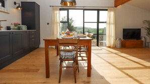 Une cuisine moderne avec des meubles de couleur sombre, une table à manger en bois et une grande fenêtre donnant sur la campagne.