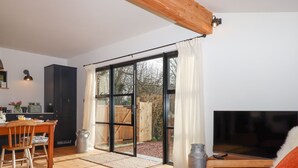 Un vaste espace de vie doté d’un plancher en bois, d’un téléviseur, d’un canapé avec un coussin moelleux, d’une table à manger avec des chaises et d’un coin cuisine avec une fenêtre et des rideaux.