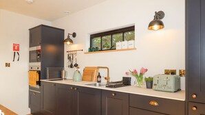 Une cuisine moderne avec des meubles de couleur sombre, un plan de travail en bois, un four encastré, une bouilloire et un grille-pain de style vintage.