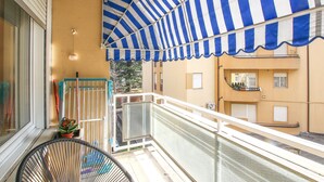 A balcony with a striped awning, a chair, a potted plant, and a building in the background. - 3 bedroom nice apartment in Rovereto (Rovereto)