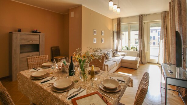 A dining area with a table set for four, a sofa, and a television in a living room. - 3 bedroom nice apartment in Rovereto (Rovereto)