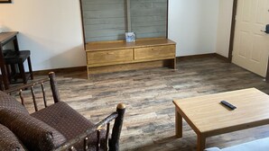 Ein Wohnzimmer mit einer hölzernen Bank, einem an der Wand montierten Fernseher und einem Holztisch.