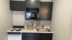 Cocina compacta con estufa, microondas, pileta y muebles oscuros.
