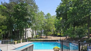 Une piscine entourée d’arbres, avec une clôture et un panneau indiquant les règles d’utilisation de la piscine.