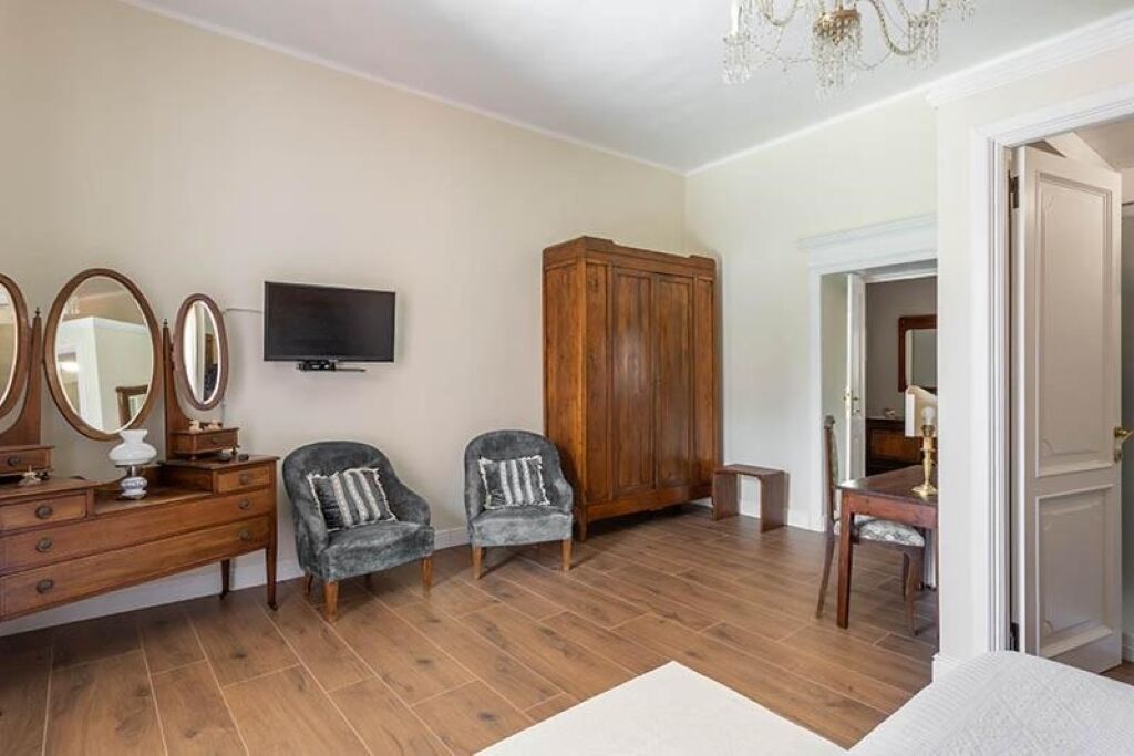 A bedroom with a wooden dresser, two armchairs, a television, and a wardrobe.