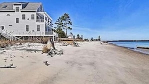Ein Strandgrundstück mit einem großen Haus, einer überdachten Veranda und einem Sandstrand.