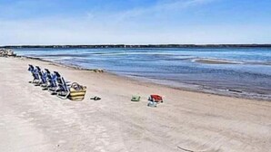 Ein Strand mit mehreren Booten, die am Sand liegen, ein Steg im Hintergrund und ruhigem Meer.