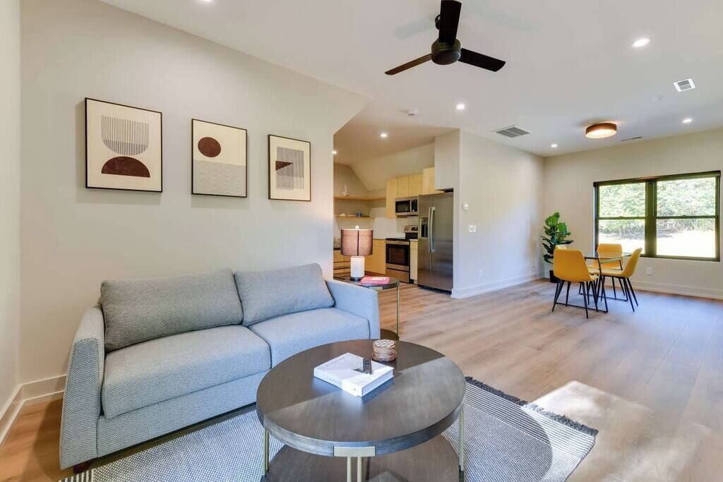 A modern living room with a grey sofa, a round coffee table, and a dining area with yellow chairs.