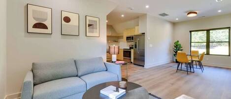 A modern living room with a grey sofa, a round coffee table, and a dining area with yellow chairs.
