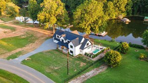 A large house with a swimming pool, surrounded by a well-maintained lawn and a lake. - Spacious Lakefront Retreat, Enjoy Dock and Pool (Mooresville)