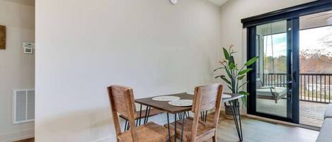 Een eethoek met een tafel, stoelen, een potplant en een schuifdeur naar een buitenbalkon.