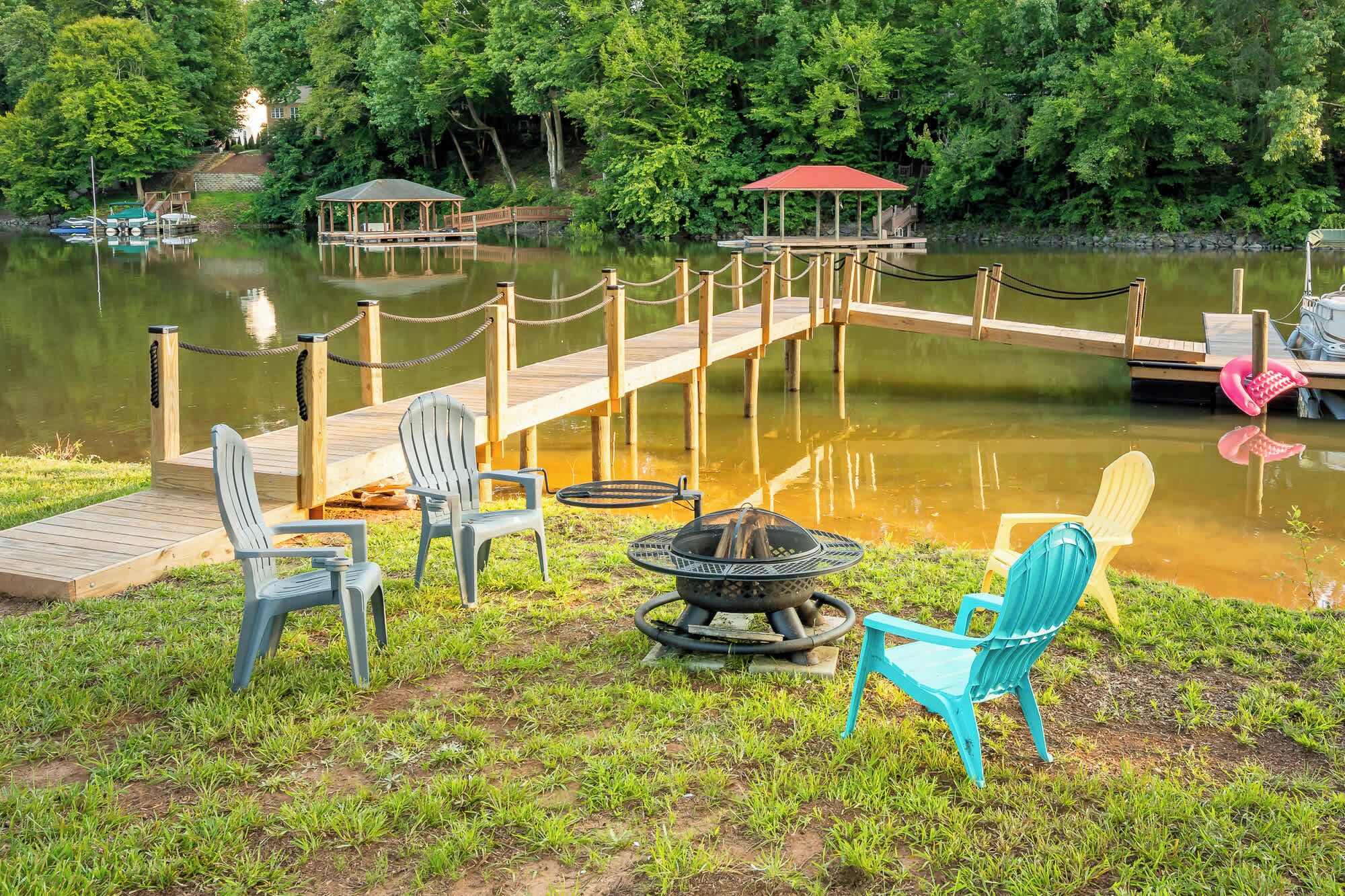 A lakeside deck with chairs, a fire pit, and a dock extending into the water.