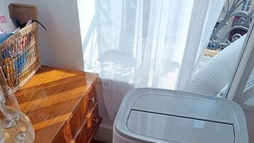 A room with a white H&B air purifier, wooden furniture, and a window with sheer curtains.