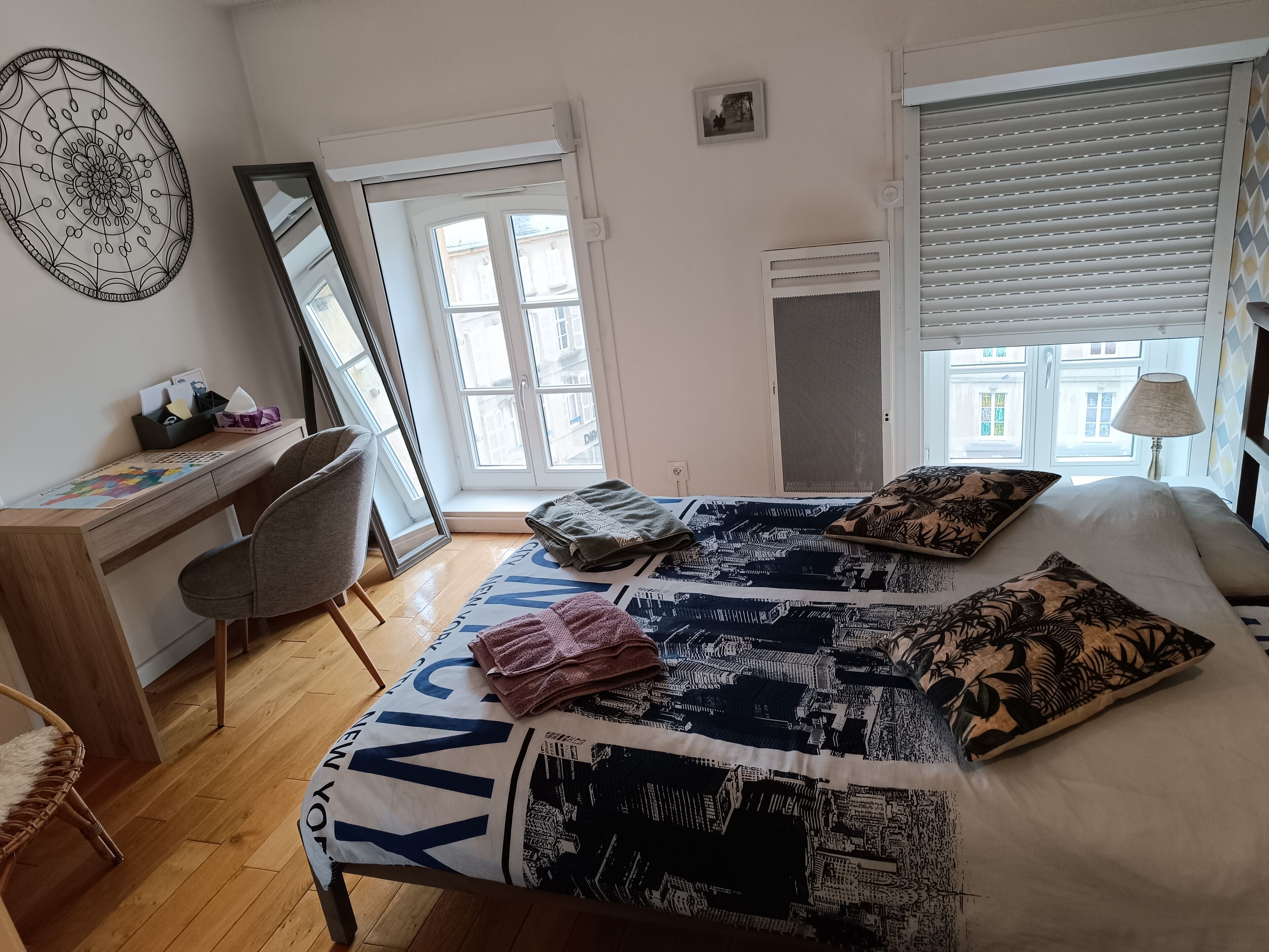 A bedroom with a bed, a desk, a chair, a window, and a wall decoration.