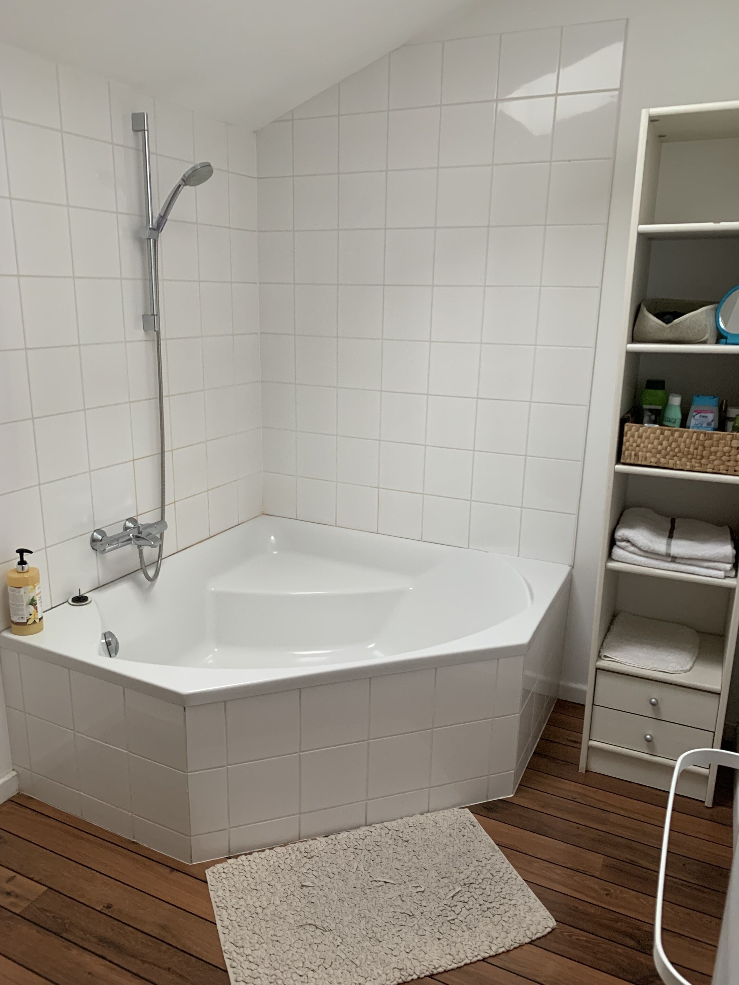 Ett badrum i ett hörn med ett fristående badkar, en dusch och en hylla med toalettartiklar.