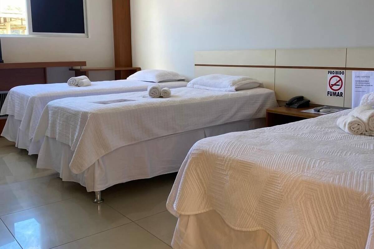 A hotel room with two beds, a window, an air conditioning unit, and a sign prohibiting smoking.