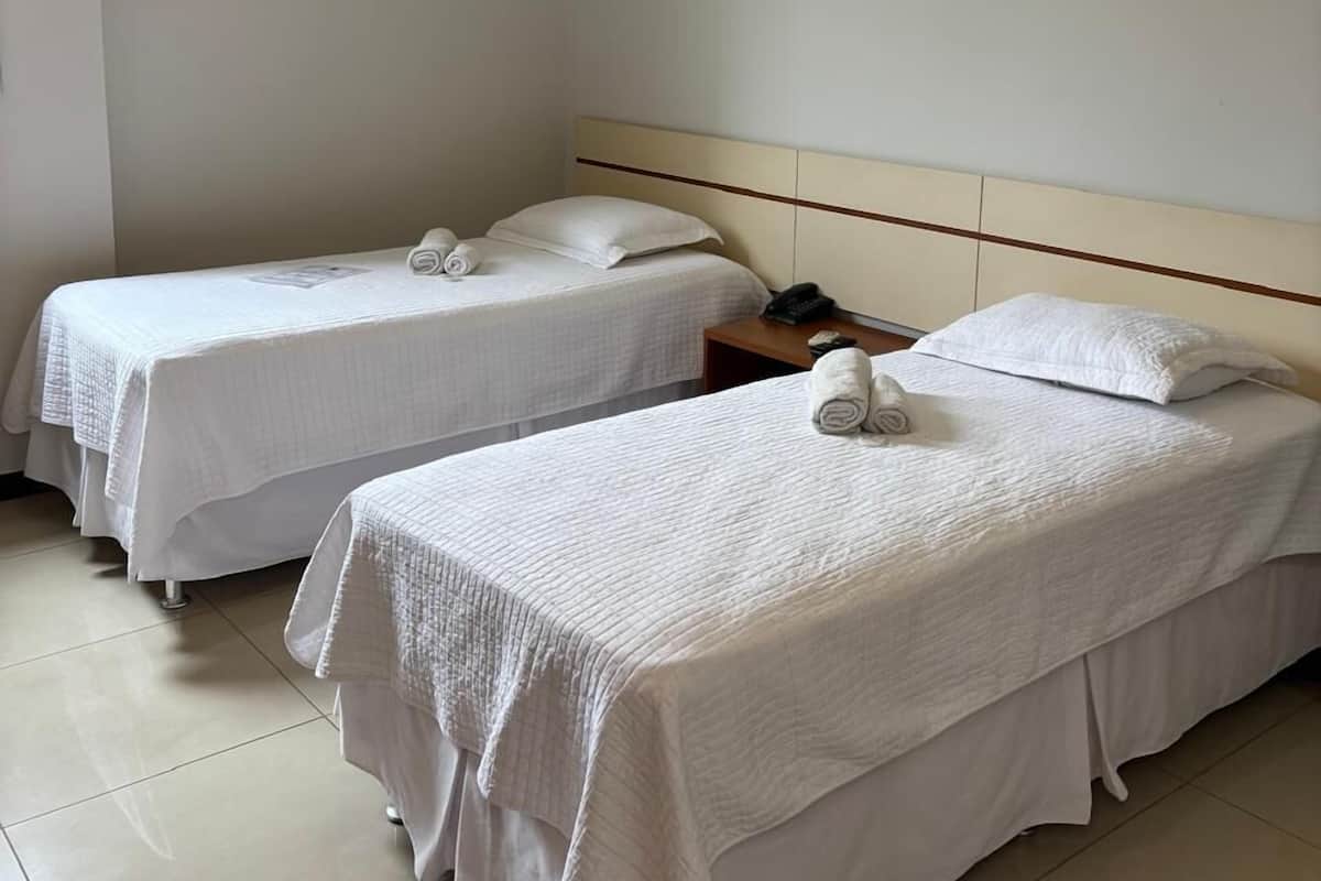 Two single beds with white bedding, a wooden nightstand with a phone, and a tiled floor.