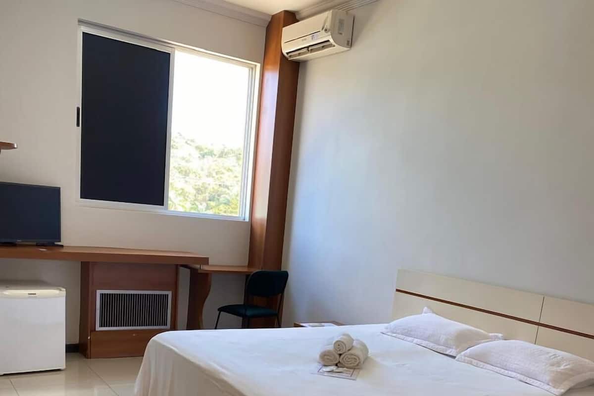 A hotel room with a bed, a desk, a chair, and a window.