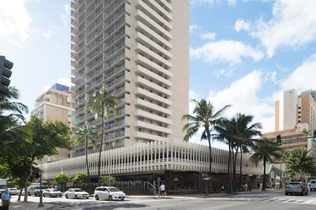 A tall hotel with a modern facade, multiple balconies, and a covered entrance area.