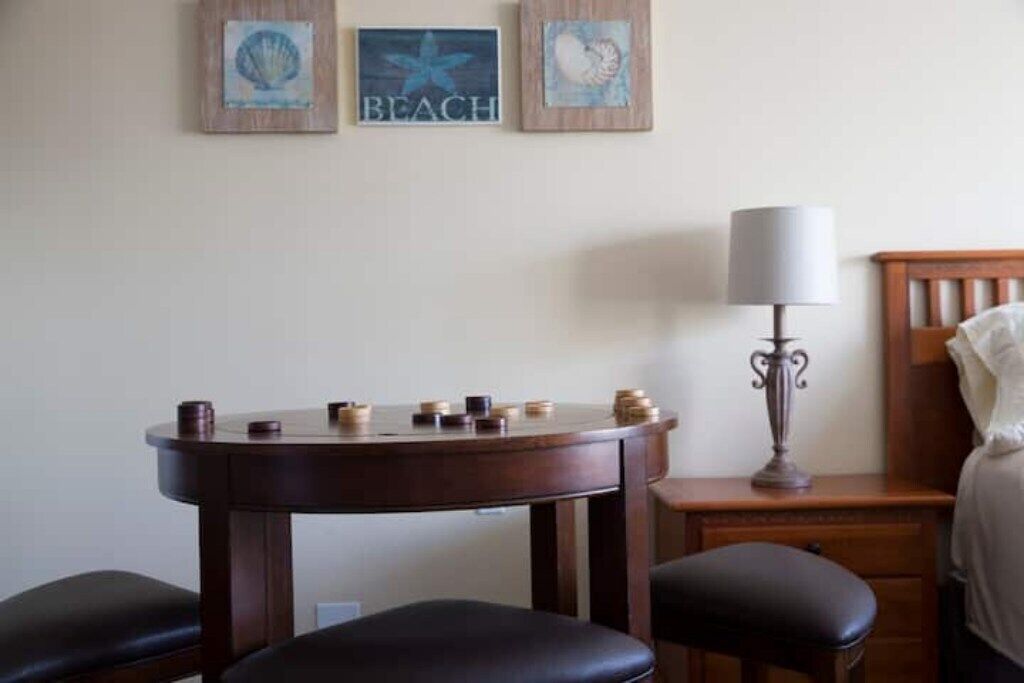 A room with a wooden table, two black leather chairs, a lamp, and three framed pictures on the wall.
