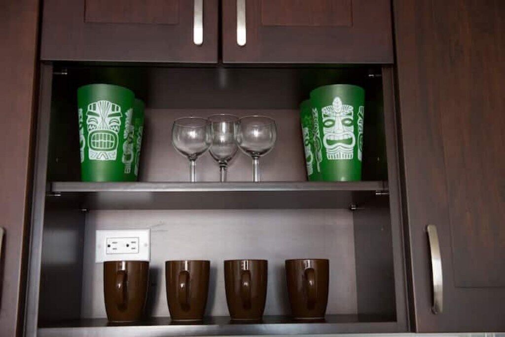 A kitchen cabinet with green containers and brown mugs.