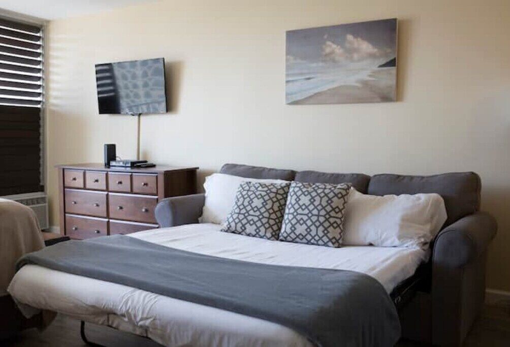 A bedroom with a bed, a dresser, a television, and a painting on the wall.