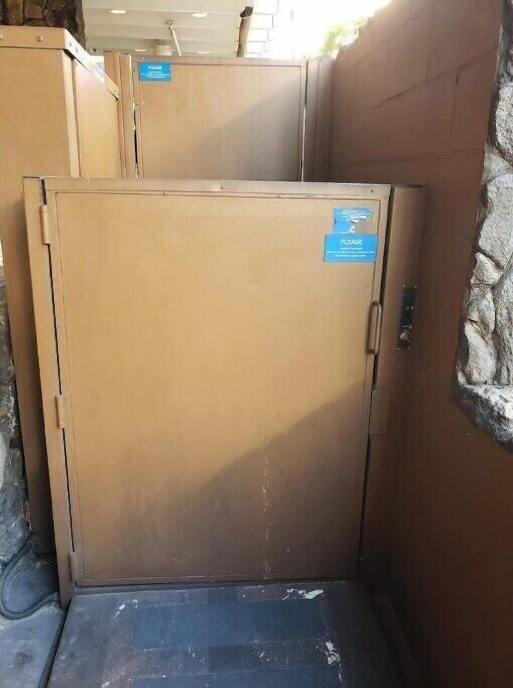 Un armario metálico grande, color beige, con un letrero azul que dice 'LEASE', ubicado en un área de paredes de piedra y piso de concreto.