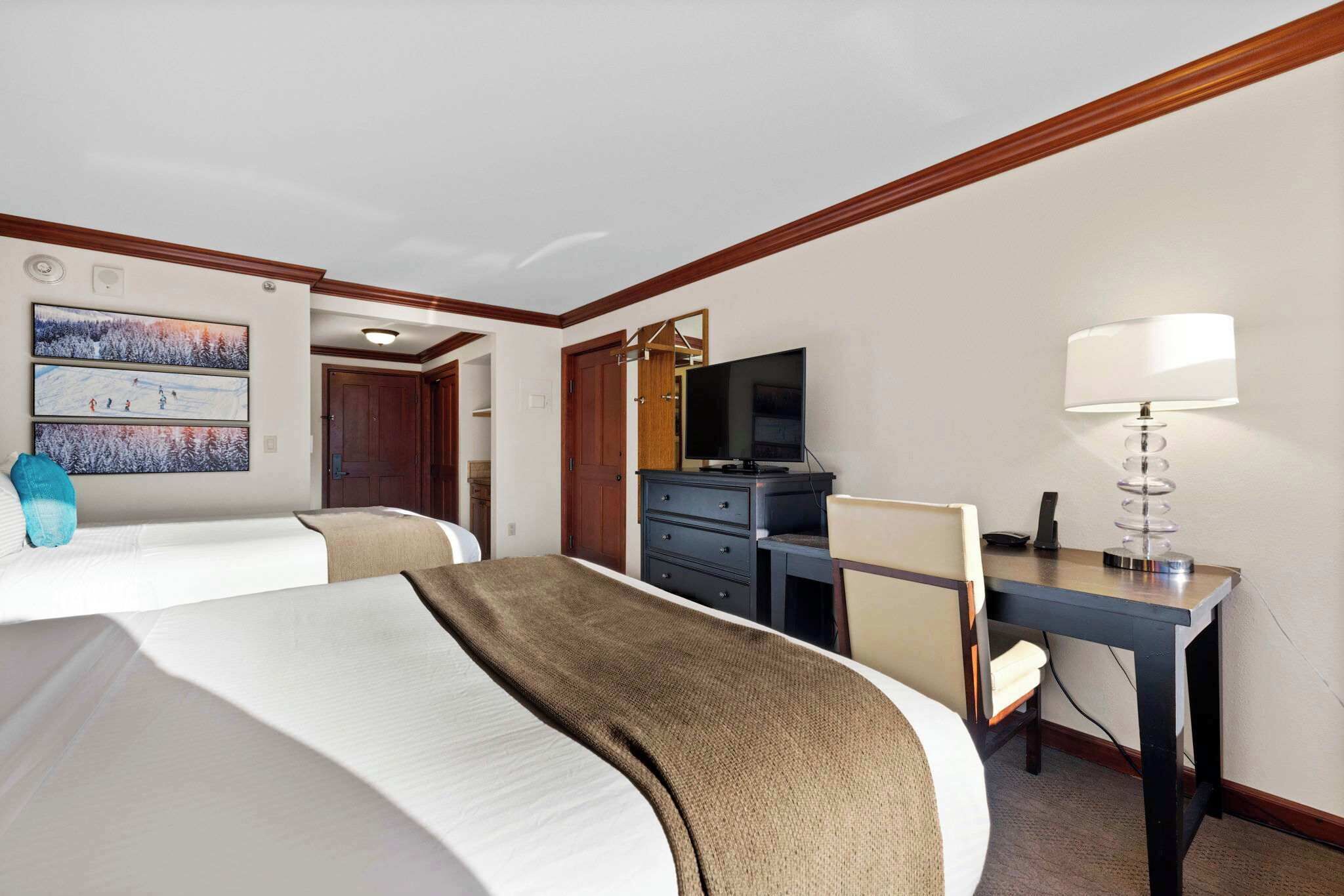 A hotel room with two beds, a desk, a television, and a lamp.