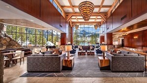 A spacious lobby with a stone fireplace, large windows offering mountain views, and a central seating area with sofas and tables. - Deluxe Forest View Studio-No Resort Fees (Olympic Valley)