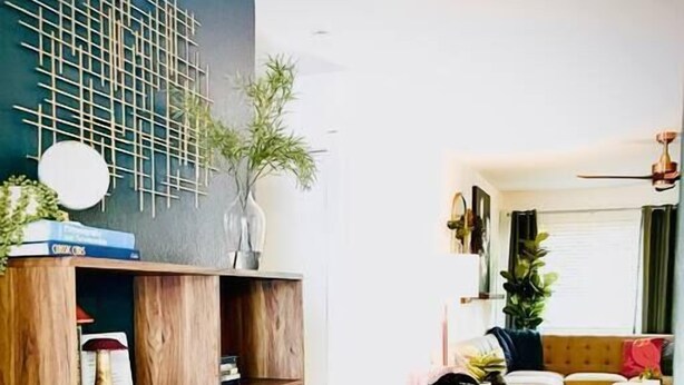 Een moderne woonkamer met een houten boekenkast, een zwarte bank en een kamerkleed met een patroon.