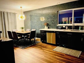 A modern kitchen with a dining area, featuring a large island, dark cabinetry, and a pendant light. - Remodeled 4BR near Maidu Park · Roseville/Granite Bay · Pets OK (Roseville)