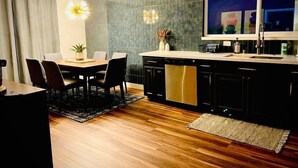 Een moderne keuken met een eethoek, met een houten eettafel, stoelen, een keukeneiland met spoelbak en een groot raam met kunstwerk.