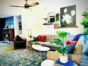 A living room with a ceiling fan, a sofa, a coffee table, and a large painting of flowers. - Remodeled 4BR near Maidu Park · Roseville/Granite Bay · Pets OK (Roseville)